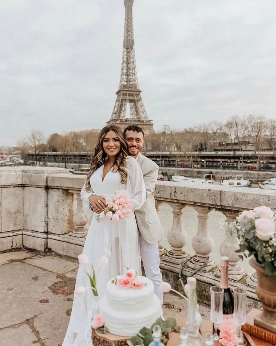 Casal com bolo e taças em terraço com a Torre Eiffel ao fundo